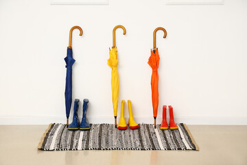Colorful umbrellas and rubber boots near light wall