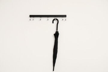 Hanger with black umbrella on light wall
