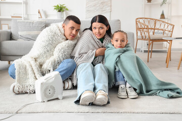 Frozen family warming near electric fan heater at home - obrazy, fototapety, plakaty