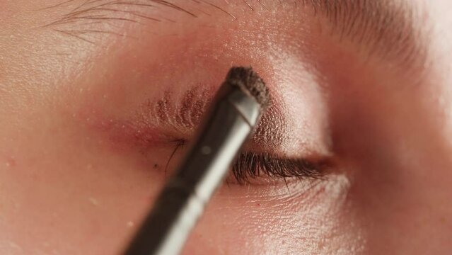 Eye shadow makeup to the upper eyelid, close-up. Makeup artist applies a bright eye shadow with a makeup brush.Tutorial master class of professional makeup. 