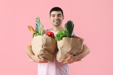 Young man with grocery bags on pink background