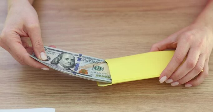 Businesswoman hands putting hundreds of dollars into paper envelope closeup