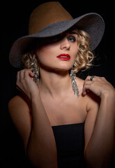Fototapeta na wymiar Sexy fashionable woman in an elegant hat and black dress. Mysterious blonde in retro style on a black background.