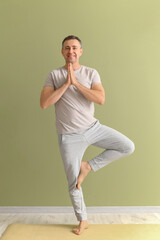 Mature man doing yoga on mat near green wall