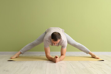 Mature man practicing yoga on mat near green wall