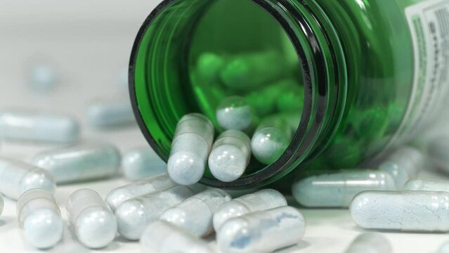 Capsules with blue powder scattered on the table. Open green container for nutritional supplements lies on the table. In reality these are tablets of copper in chelated form