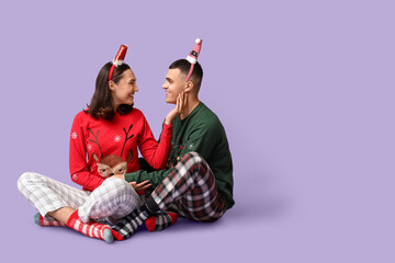 Happy young couple in Christmas pajamas on lilac background