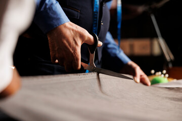 Fashion industry specialists manufacturing suit in atelier workspace, cutting textile material with scissors for upcoming bespoke collection. Process of making clothes in luxury tailoring studio