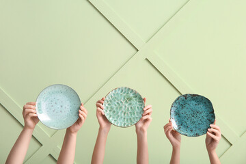 Female hands with plates against color wall
