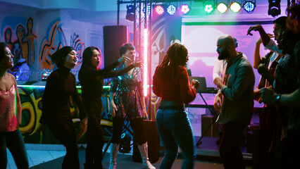 Funky persons doing dance battle to show off electronic music at discotheque, having fun at cool disco party with dancers. Happy people improvising breakdance battle at event. Handheld shot.