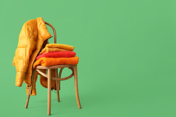 Stacked sweaters with jacket on chair against green background