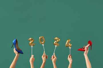 Female hands with shoes and figure 2024 on green background. New year shopping concept