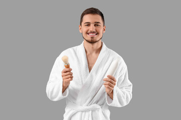 Handsome young man in bathrobe with shaving brush on grey background