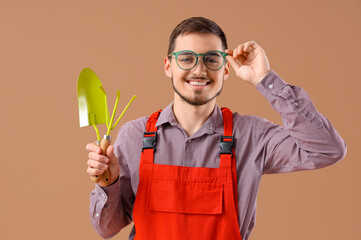 Young male gardener in eyeglasses with gardening tools on beige background