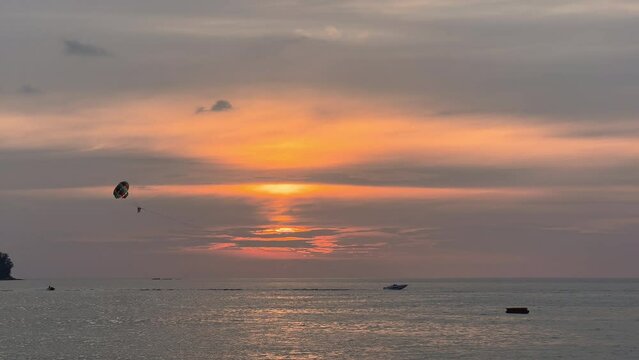 The coast of Thailand on a sunset, beach entertainment - parachute behind a motorboat, people parachute over the sea