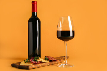 Bottle and glass of red wine with snacks on orange background