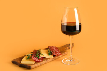 Glass of red wine with snacks on orange background