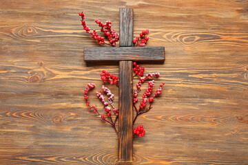 Cross with berry branches on wooden background. Christmas story concept