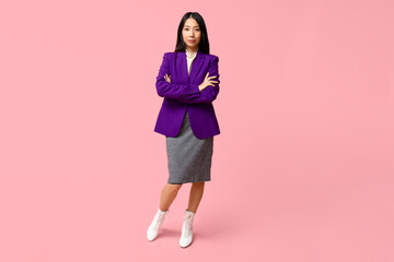 Portrait of young Asian businesswoman with crossed arms on pink background