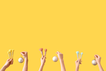 Hands holding makeup brushes and Christmas decorations on yellow background