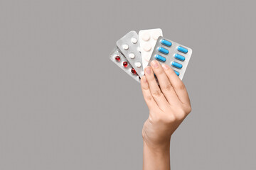 Female hand holding pills in blister packs on grey background