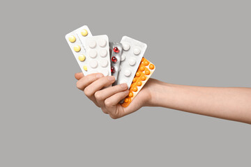 Female hand holding pills in blister packs on grey background