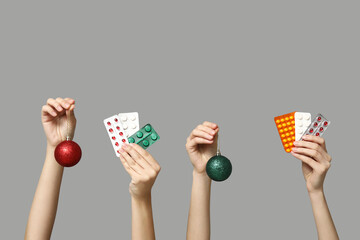 Female hands holding pills in blister packs and Christmas baubles on grey background - obrazy, fototapety, plakaty