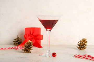 Glass of tasty red margarita with Christmas decor on table against white grunge background