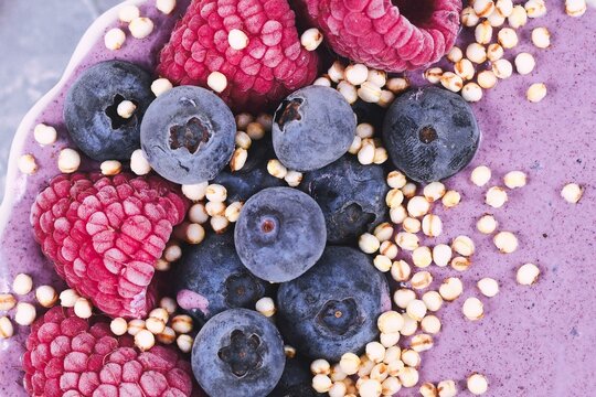 Close up of healthy yogurt and fruit smoothie bowl decorated with raspberry, blueberry and puffed quinoa grain