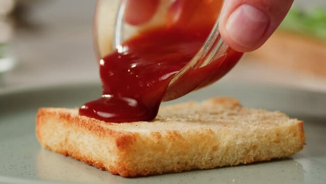 Adding red sauce jam on fried bread close-up. Cooking sandwich at cafe. Pouring tomato sauce on top. Food concept