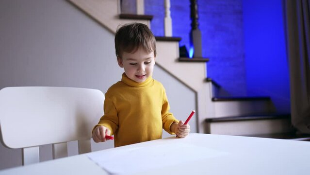 Charming baby in yellow sweater comes up to a desk holding a pen. Child moves the pen by the paper and sneezes funnily.