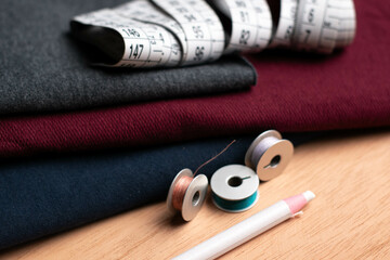 texture of dark red, dark blue and dark gray fabrics, white pencil, spools and plastic meter of threads on a wooden table - obrazy, fototapety, plakaty