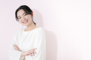 Fototapeta premium カメラ目線で白いカジュアルな服を着た笑顔の若い女性の上半身 ピンクの背景