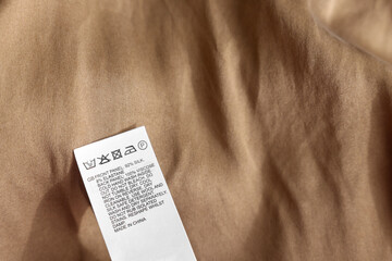 Clothing label in different languages on beige garment, closeup