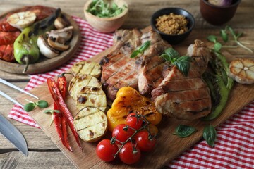 Delicious grilled meat and vegetables served on wooden table, closeup