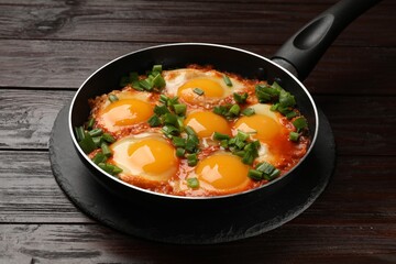Delicious shakshuka in frying pan on wooden table, closeup
