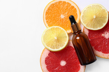 Bottle of cosmetic serum and sliced citrus fruits on white background, flat lay. Space for text