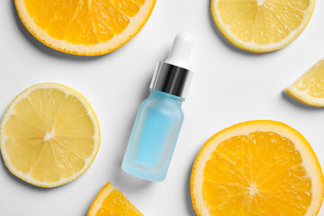 Bottle of cosmetic serum and sliced citrus fruits on white background, flat lay