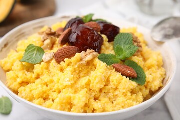 Tasty cornmeal with dates, nuts and mint in bowl on white table, closeup