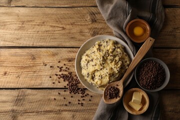 Chocolate chip cookie dough in bowl and ingredients on wooden table, flat lay. Space for text
