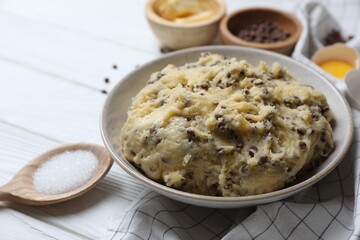 Chocolate chip cookie dough in bowl and ingredients on white wooden table