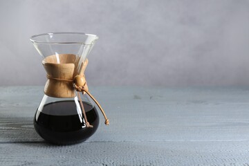 Glass chemex coffeemaker with drip coffee on grey wooden table. Space for text