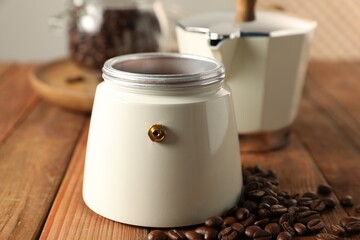 Moka pot and coffee beans on wooden table, closeup