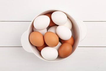 Unpeeled boiled eggs in saucepan on white wooden table, top view