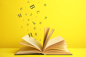 Open book with letters flying out of it on yellow background