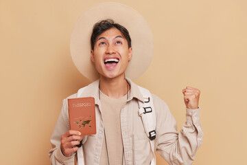 Happy oriental tourist boy showing his passport smiling widely and thanks heavens for new visa,...
