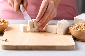 Hand holding knife and cutting tofu on wooden board, Healthy eating