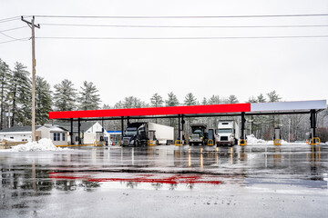 Different big rig semi trucks with semi trailers refuel tanks at a gas station on a truck stop with...