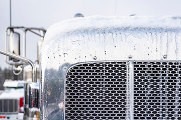 Iced chrome classic semi truck grille with snow covered top and side mirrors standing on the winter...