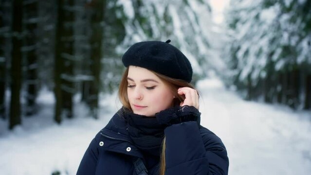 Close up shot of young caucasian female fixing her hair while looking at the snow covered forest floor at daytime.